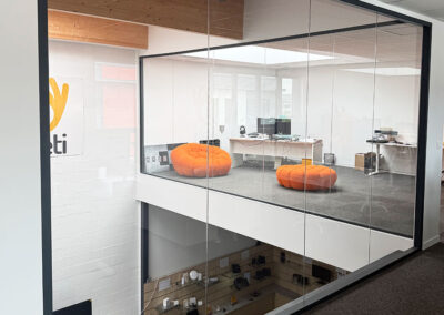 Glass-walled office area with two orange bean bag chairs and a desk with computers on the upper level